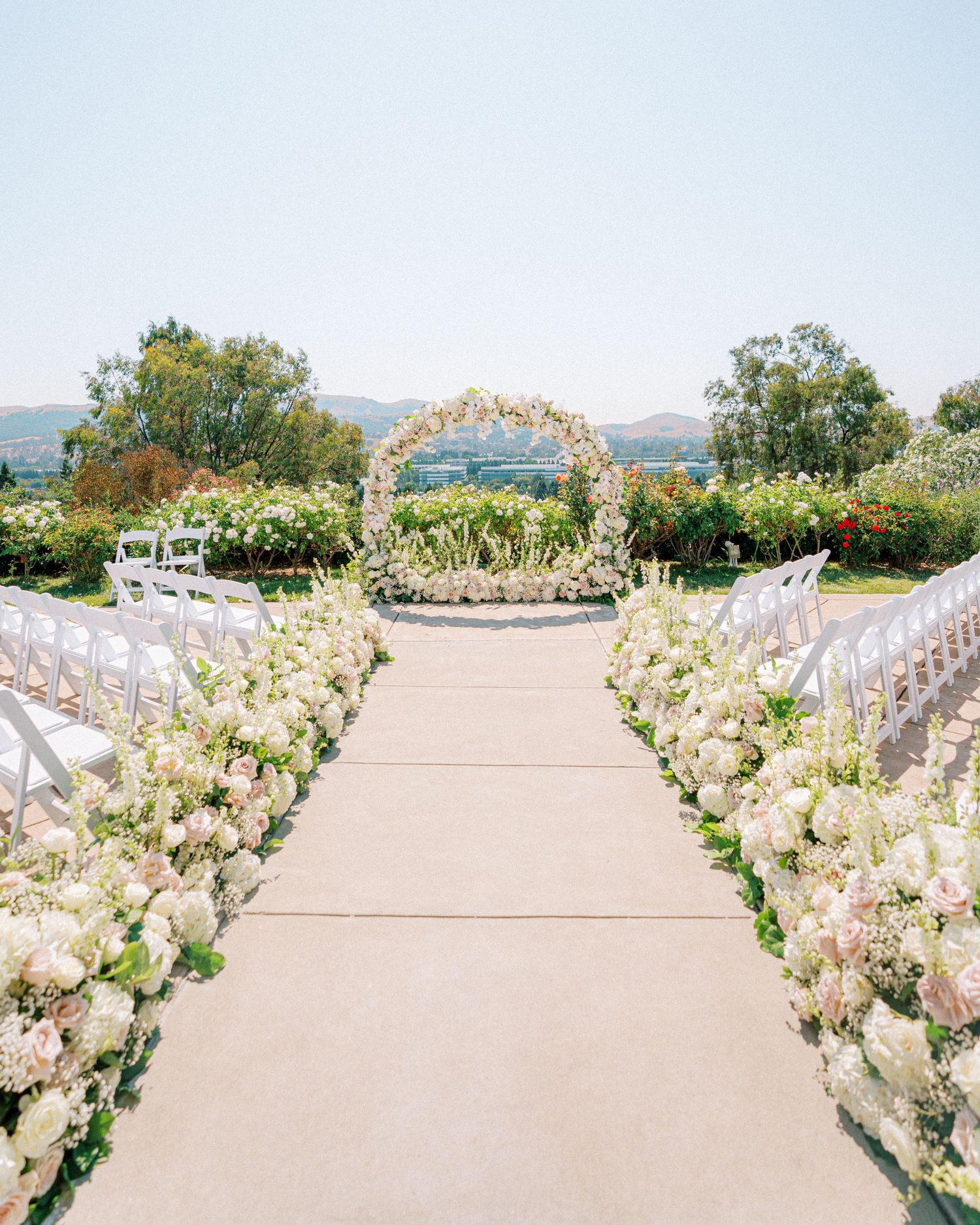 White floral-lined wedding ceremony aisle with an elegant arch overlooking mountain views.