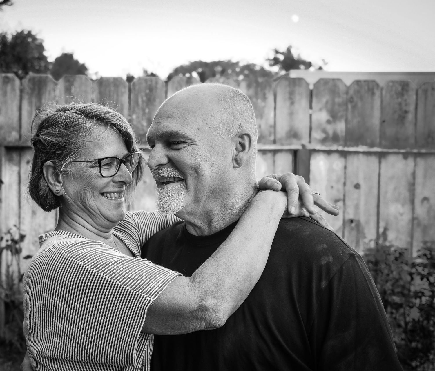 Black and white photo of a happy mature couple embracing and laughing in a backyard.