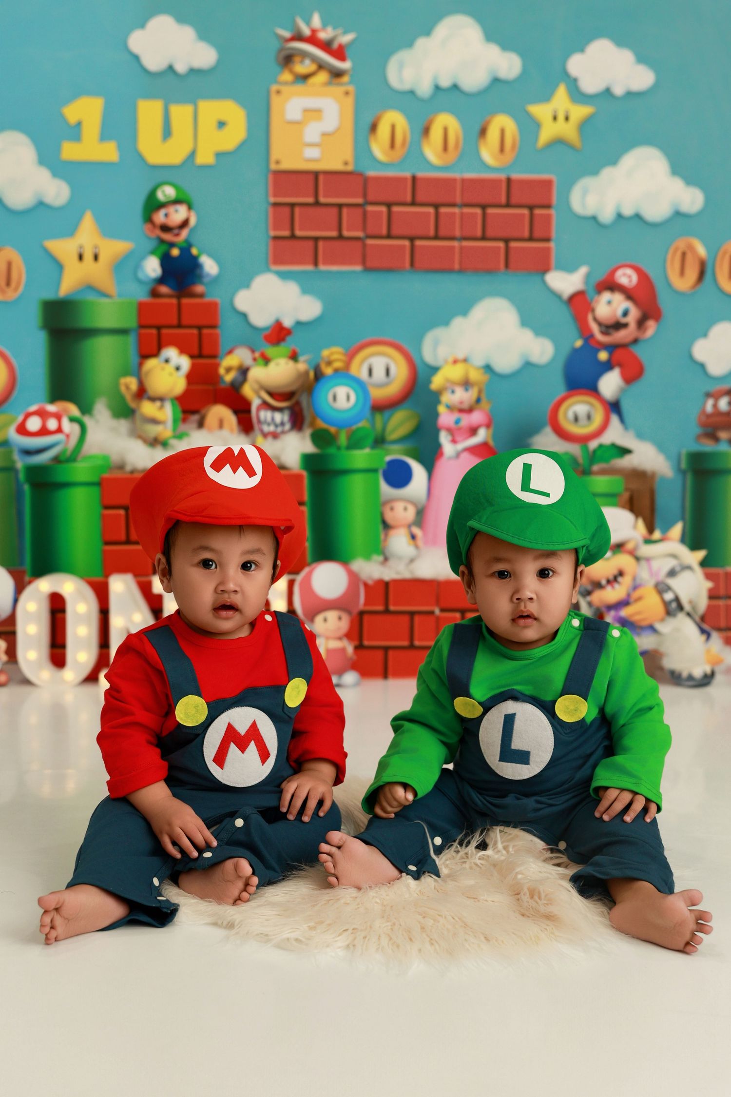 Three babies wearing Mario and Luigi themed outfits pose against a Super Mario Bros video game backdrop.