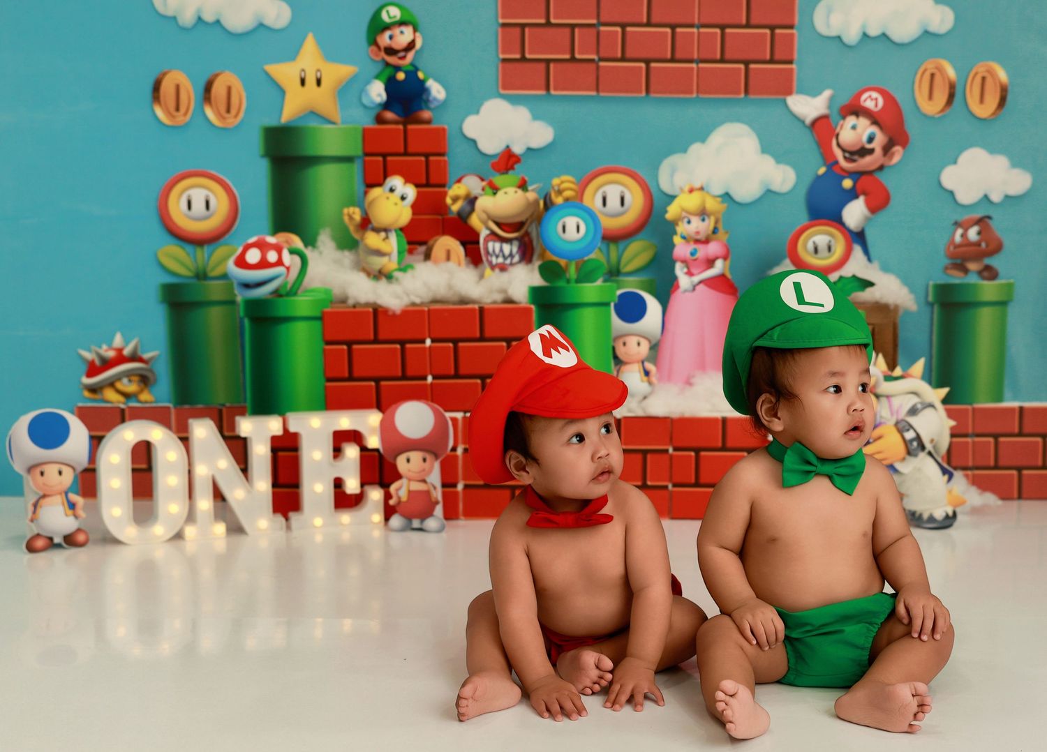 Four baby photos with Mario-themed props and decorations showing a one-year birthday milestone celebration setup.