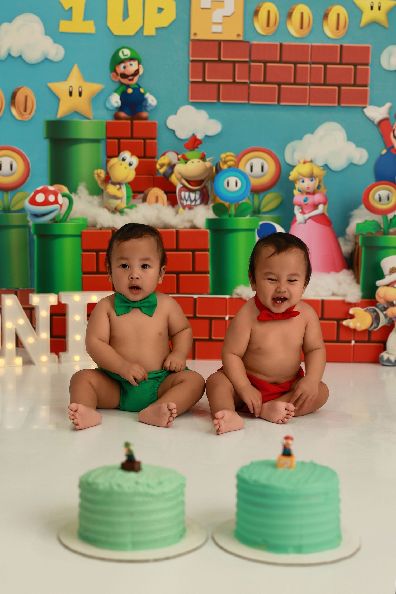 Adorable baby photoshoot with Super Mario themed backdrop featuring green pipes, brick walls, and iconic game elements.