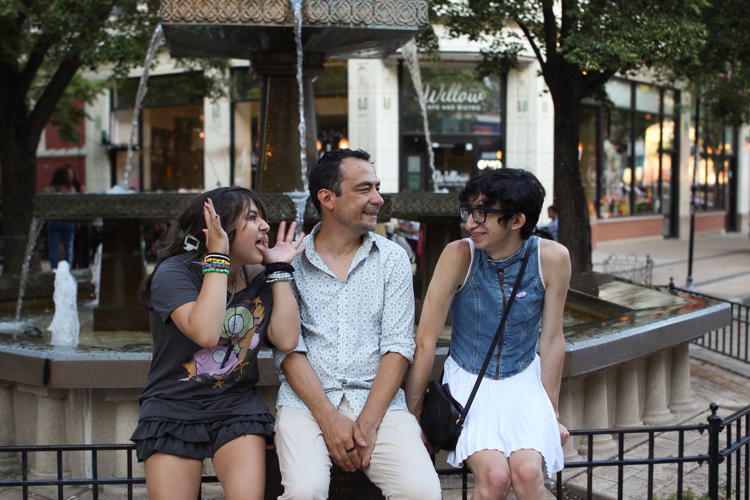 Three friends sit together on a bench in an outdoor urban setting, engaged in casual conversation.