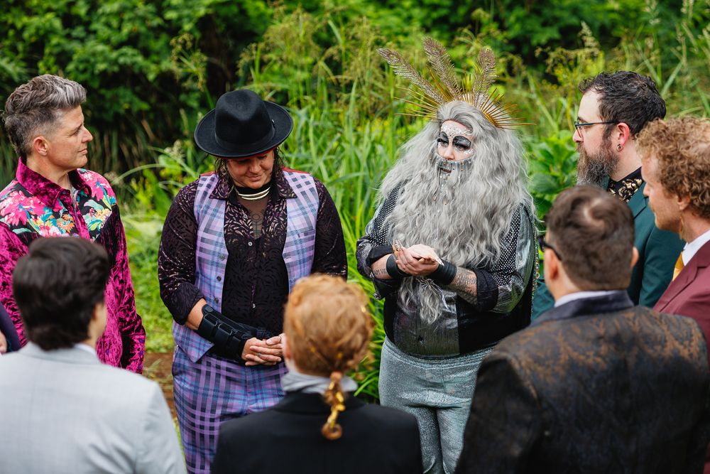 Outdoor wedding ceremony with officiant in theatrical costume and guests in colorful formal attire.