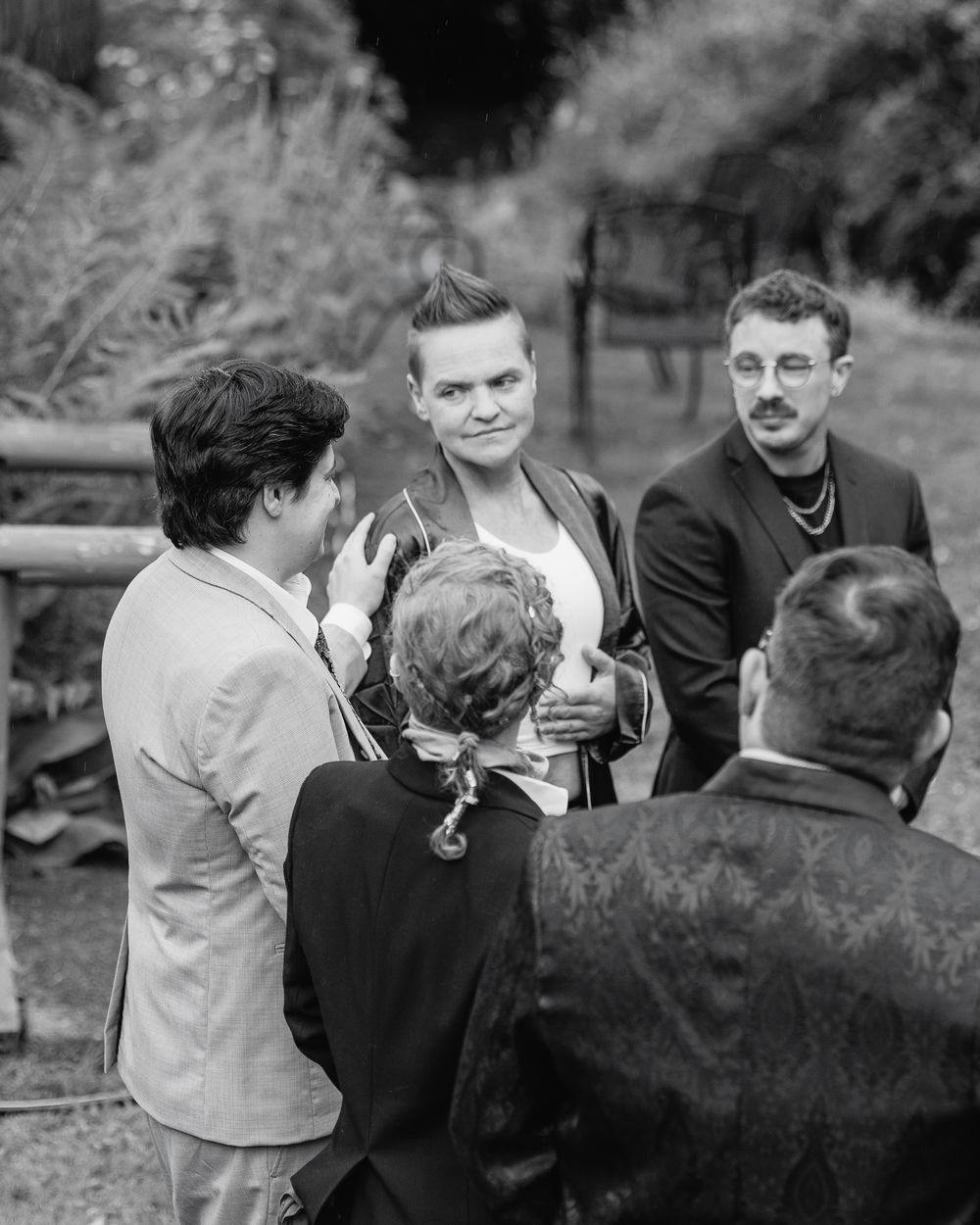 Black and white photo of wedding guests in conversation outdoors at a garden ceremony.