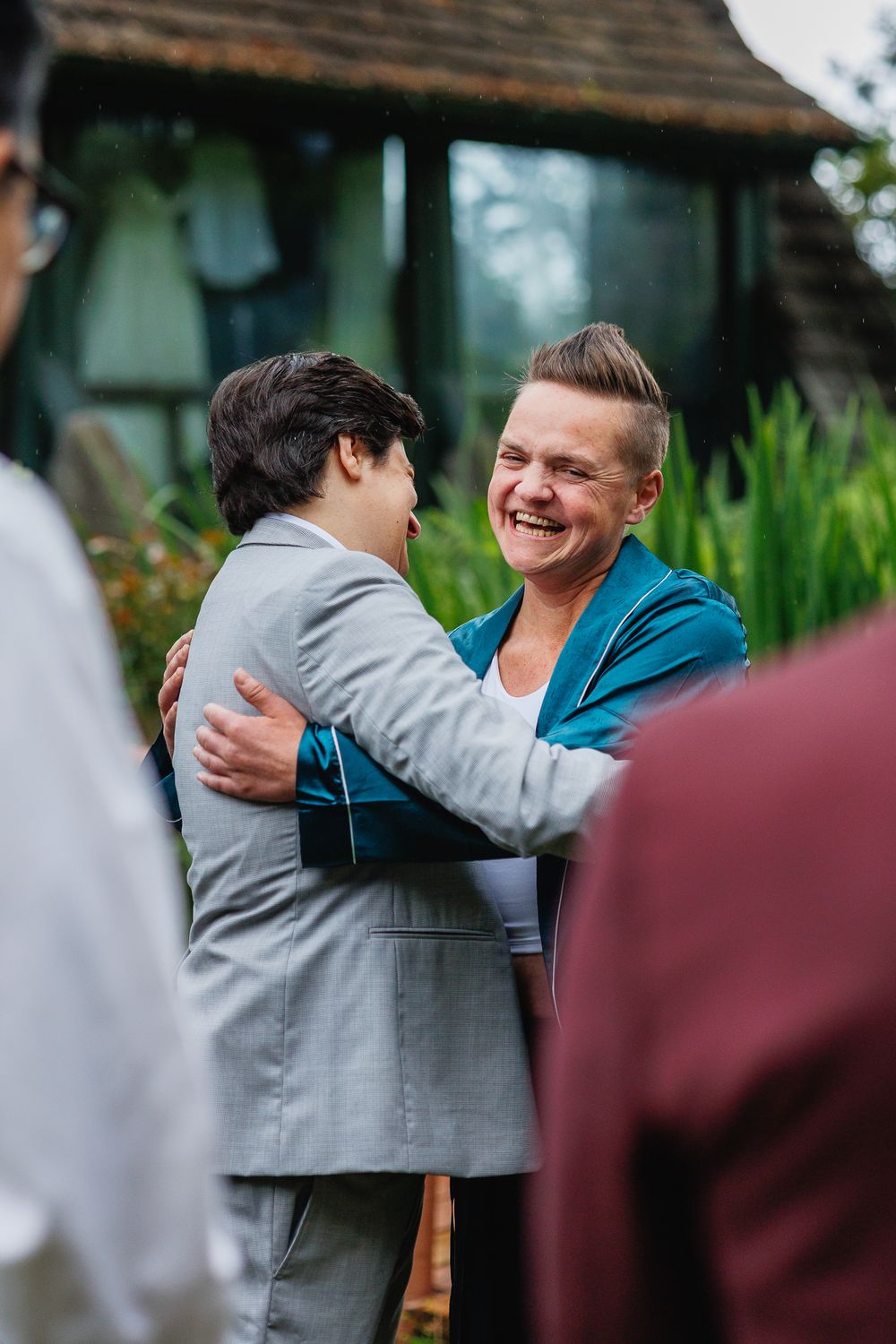 Two people sharing a warm embrace and laughing at an outdoor wedding celebration.