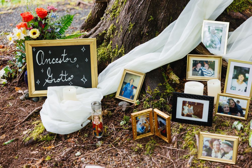 Ancestor grotto wedding display with framed photos, candles, and flowers arranged at the base of a large tree.