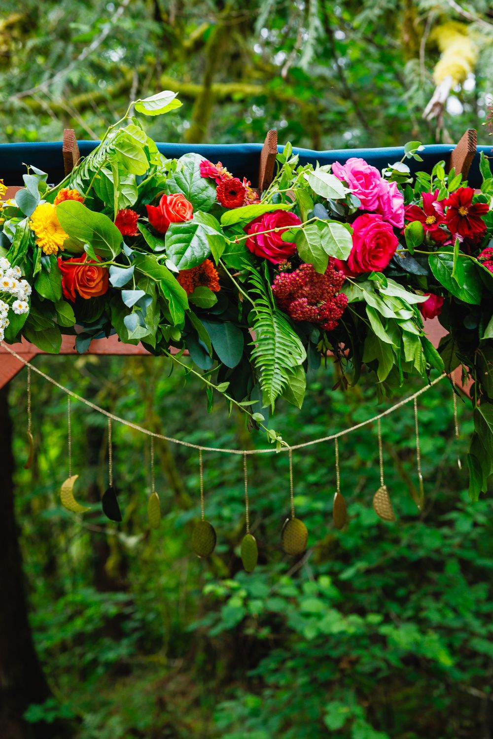 Vibrant floral arch decorated with red, pink, and orange roses and tropical greenery for wedding.