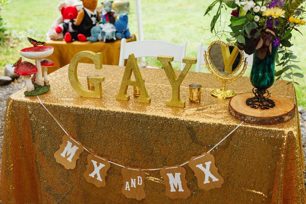 Gay wedding reception table with gold GAY letters and Mx and Mx banner on sequin tablecloth.