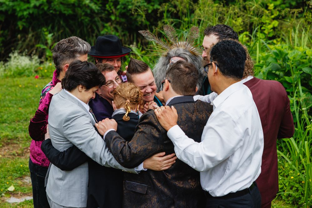 Joyful group hug among wedding guests celebrating outdoors in a lush green garden setting.
