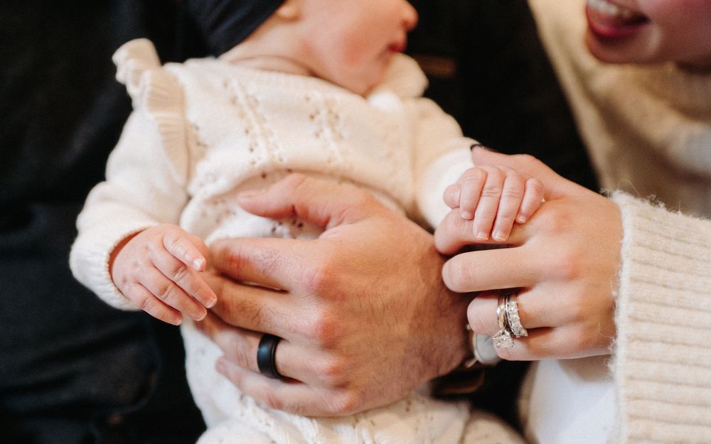 Close-up of hands wearing rings and holding a baby's hand.