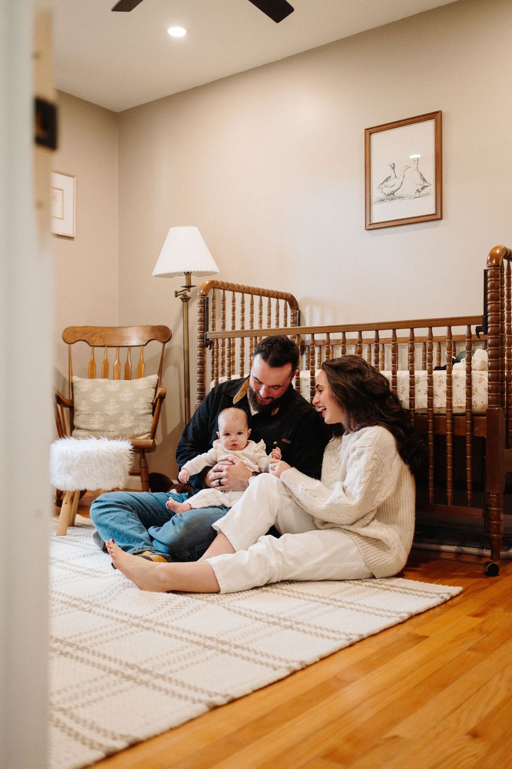 A family cuddles together on a white mattress in a cozy bedroom with hardwood floors and wooden furniture.