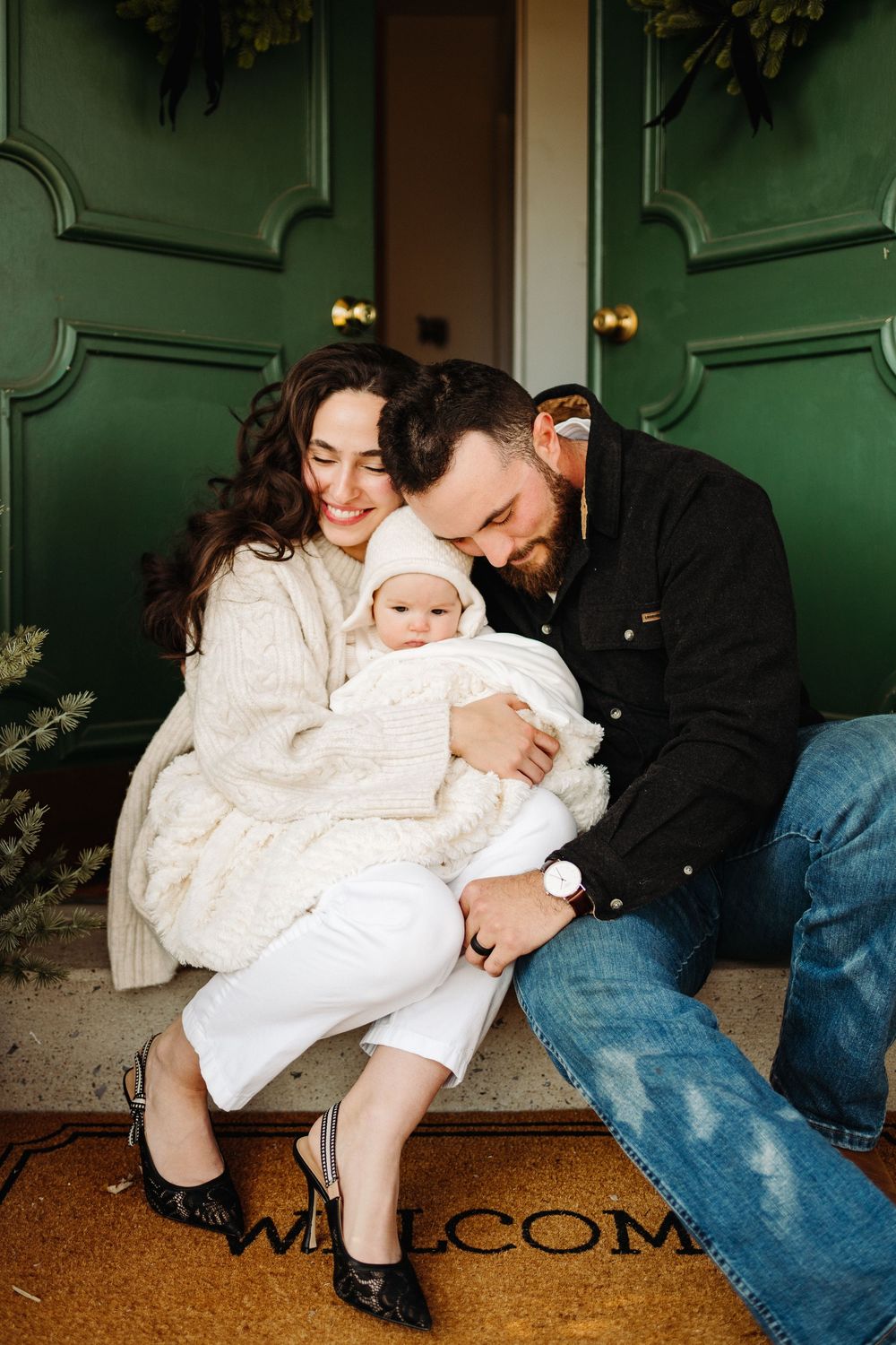Family in cozy winter outfits sitting together on a doorstep with green doors.