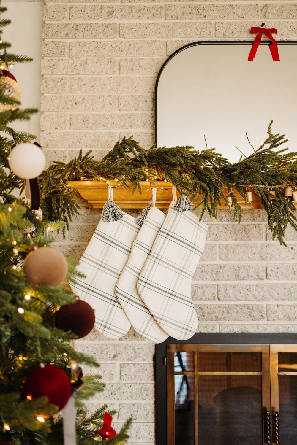 White and gray plaid stockings hang from a rustic mantel decorated with evergreen garland and Christmas ornaments.