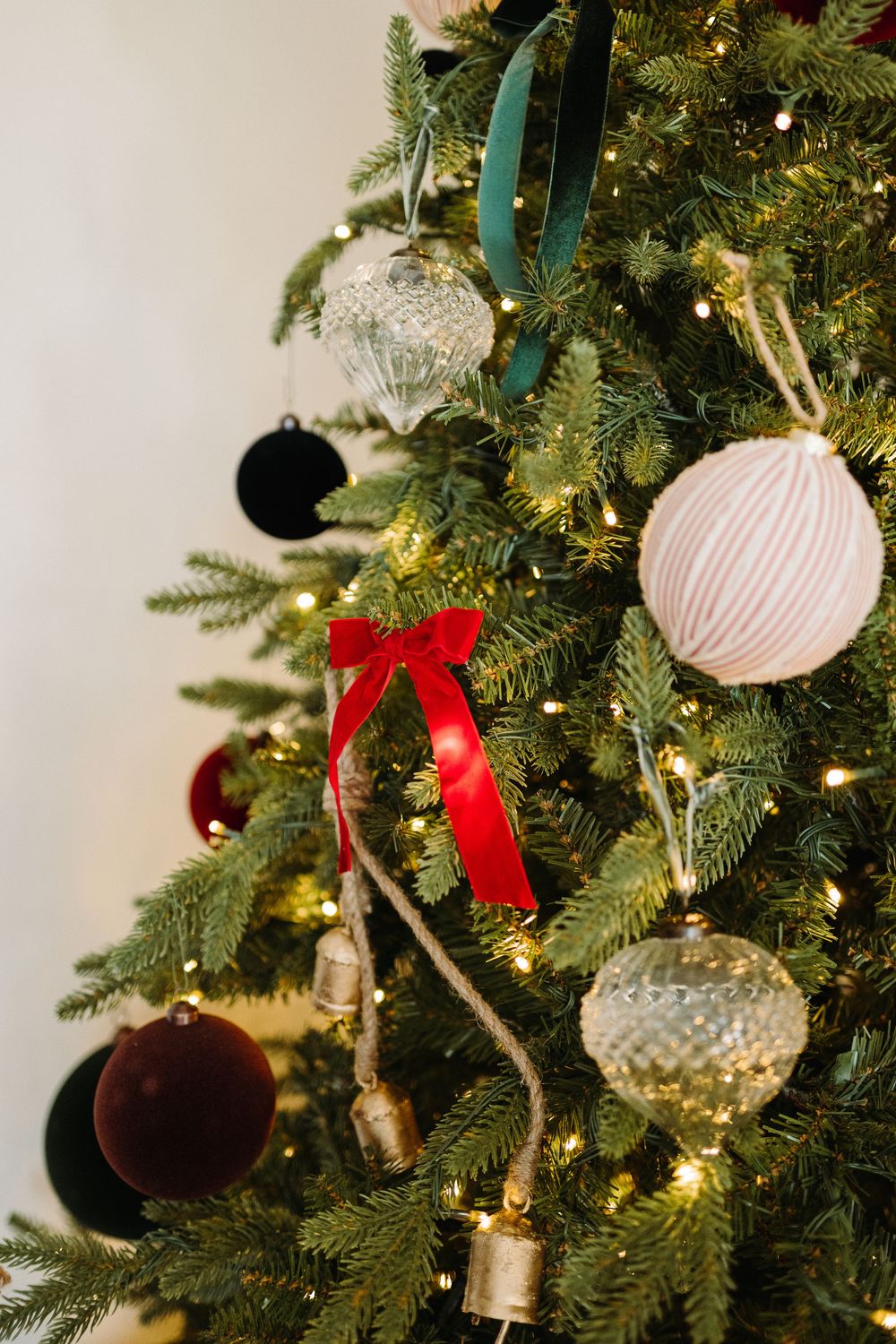 Close-up of decorated Christmas tree with glass ornaments, red bow, and twinkling lights.