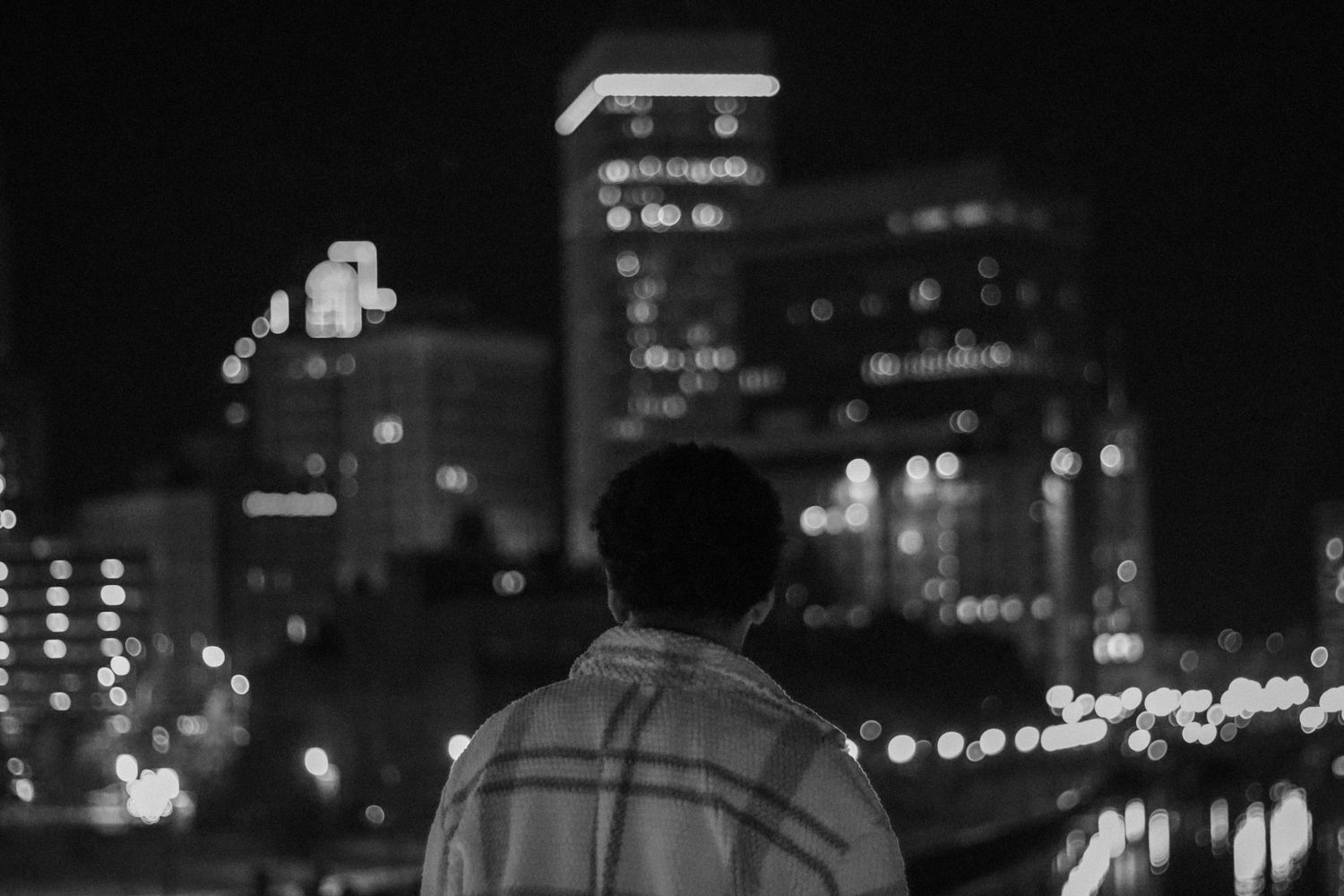 Silhouette of person looking at city skyline at night with illuminated buildings in background.