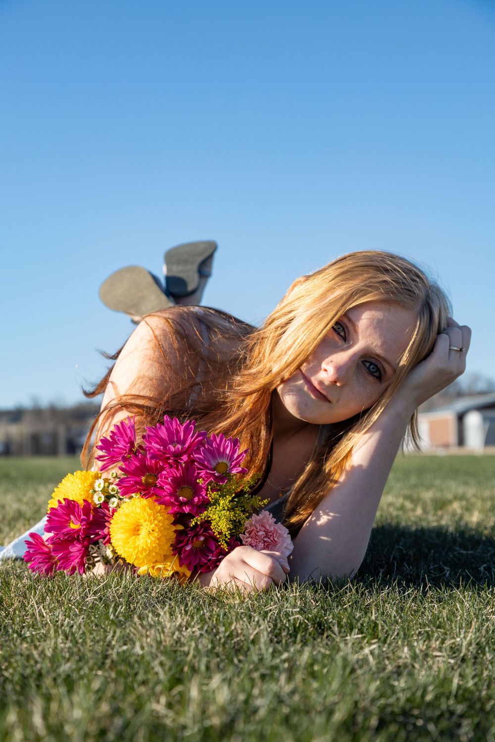 Senior poses outdoor during the spring soaking up the sun wile laying in the grass with flowers.