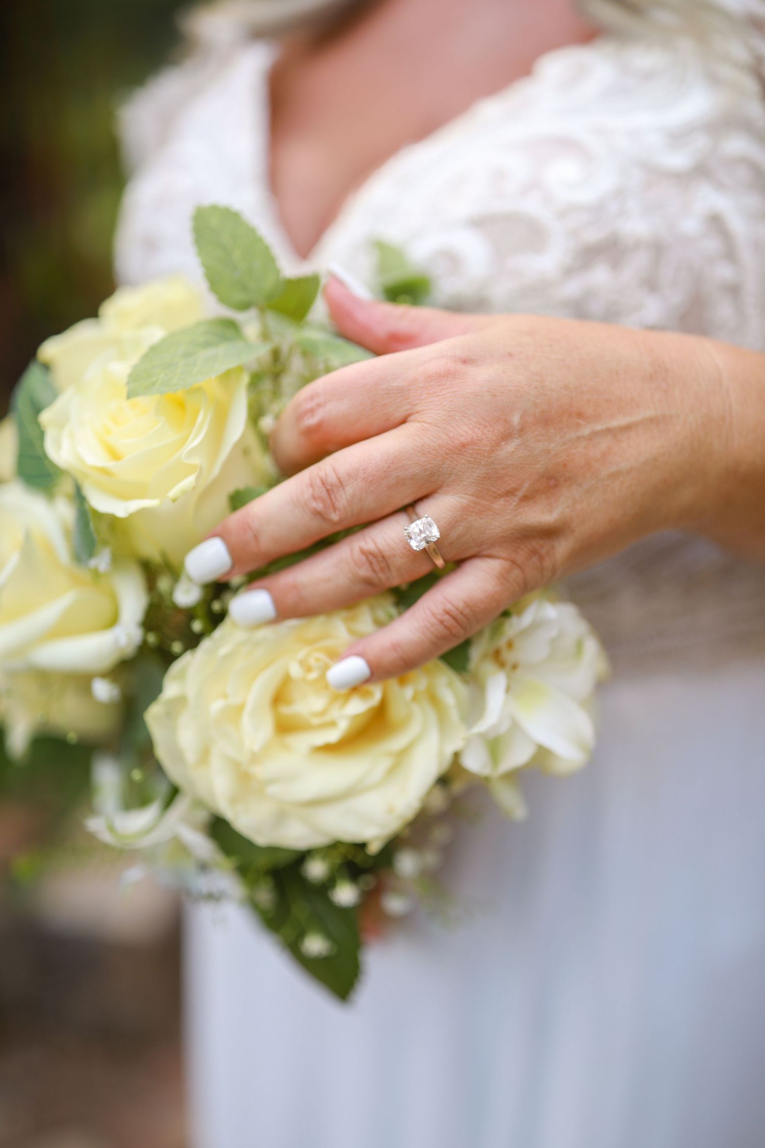 Close-up of hands with an engagement ring holding pale yellow roses.