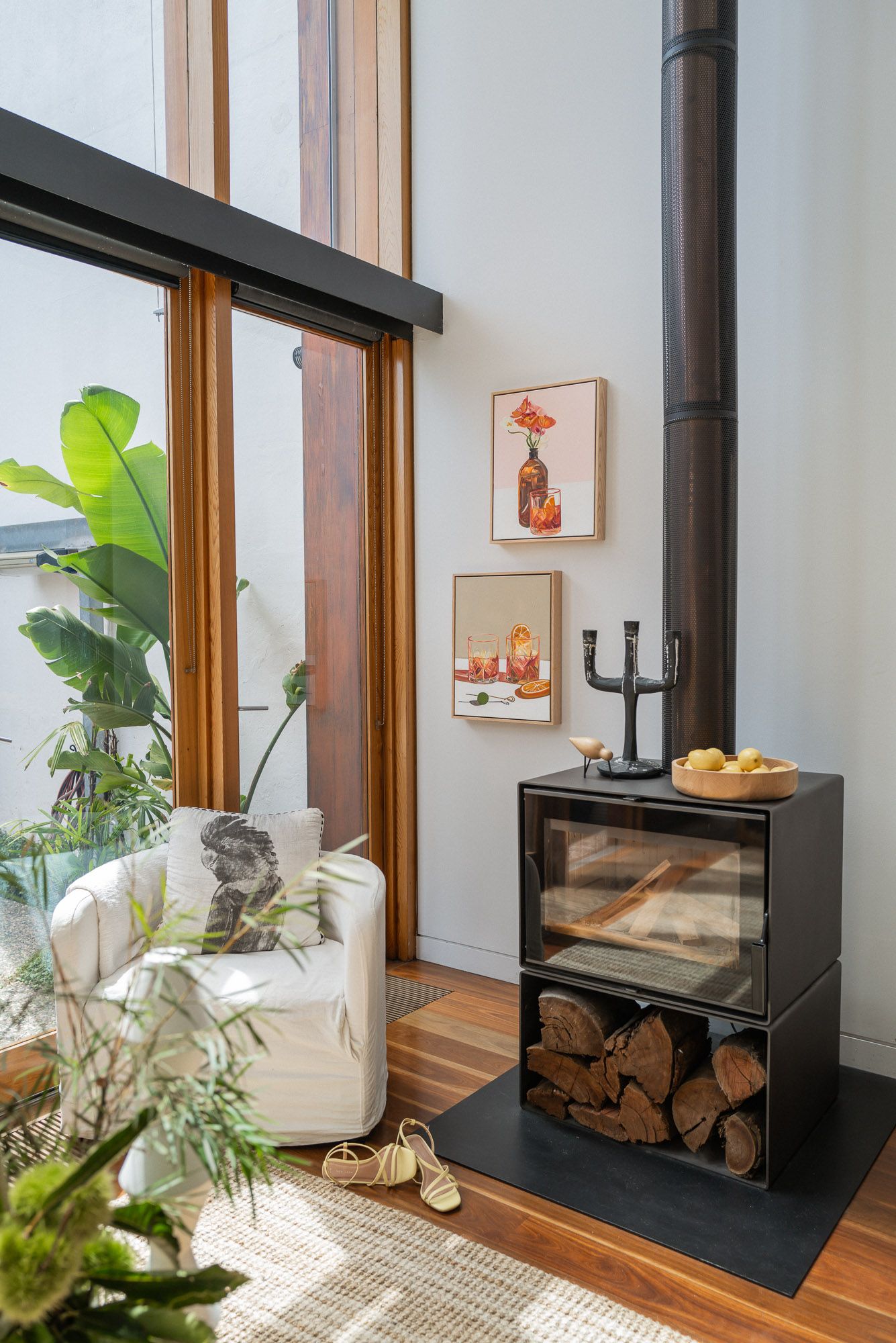Modern living room with black wood-burning stove, firewood storage, and colorful framed artwork.