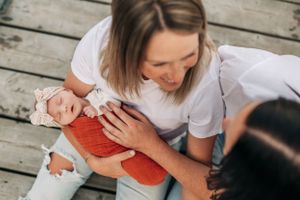 Candid moment of people interacting with baby in orange wrap on wooden dock.