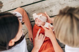 Overhead view of people tending to baby in orange wrap on weathered wooden dock.
