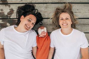 Family portrait on wooden deck with baby in orange outfit and matching headband.