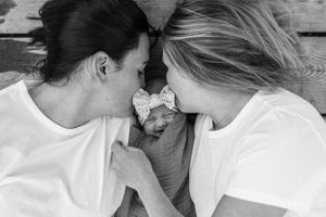 A tender black and white portrait of a newborn baby wearing a bow between two people in white shirts.