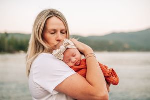 A peaceful moment with a sleeping baby in orange swaddle and bow being cradled outdoors by the water.