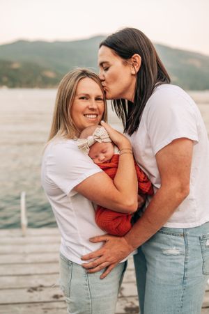 An intimate family moment with a newborn in orange wrap on a dock by the lake.