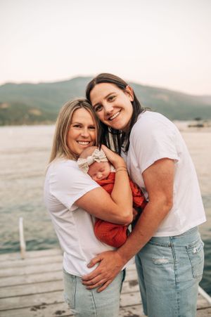 A happy outdoor portrait with a newborn in orange wrap on a wooden dock.
