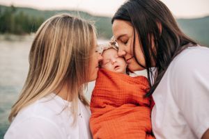A tender moment of affection with a sleeping newborn wrapped in orange between two people.