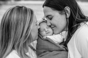 A black and white intimate portrait with a sleeping newborn being embraced by two people.