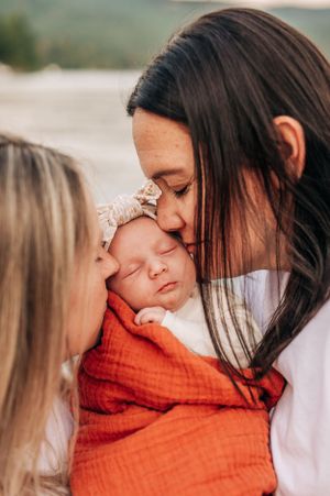 A close-up portrait showing tender affection with a sleeping baby in orange wrap and bow headband.