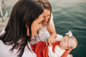 Intimate family moment with a newborn baby in red clothing on a wooden dock by the water.