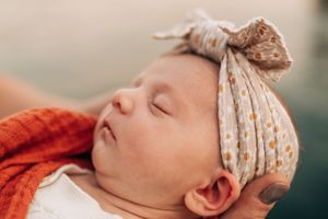Peaceful sleeping infant wearing a patterned headband and orange wrap.