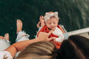 Baby in red outfit and bow resting on dock by lake.