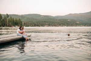 Scenic lake view with people and dog relaxing on wooden dock surrounded by mountains.