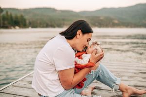 Tender moment shared with baby in red clothing on dock by lake.
