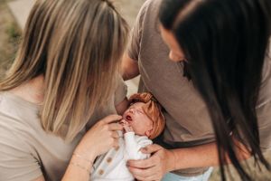 A tender moment with a newborn baby wrapped in white being held and cared for by adults.