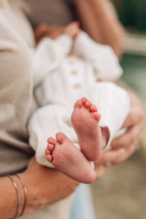 Close up of tiny newborn baby feet against white blanket with adult hands gently holding.