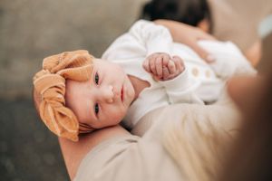 A baby wearing white clothing and orange headband rests peacefully.