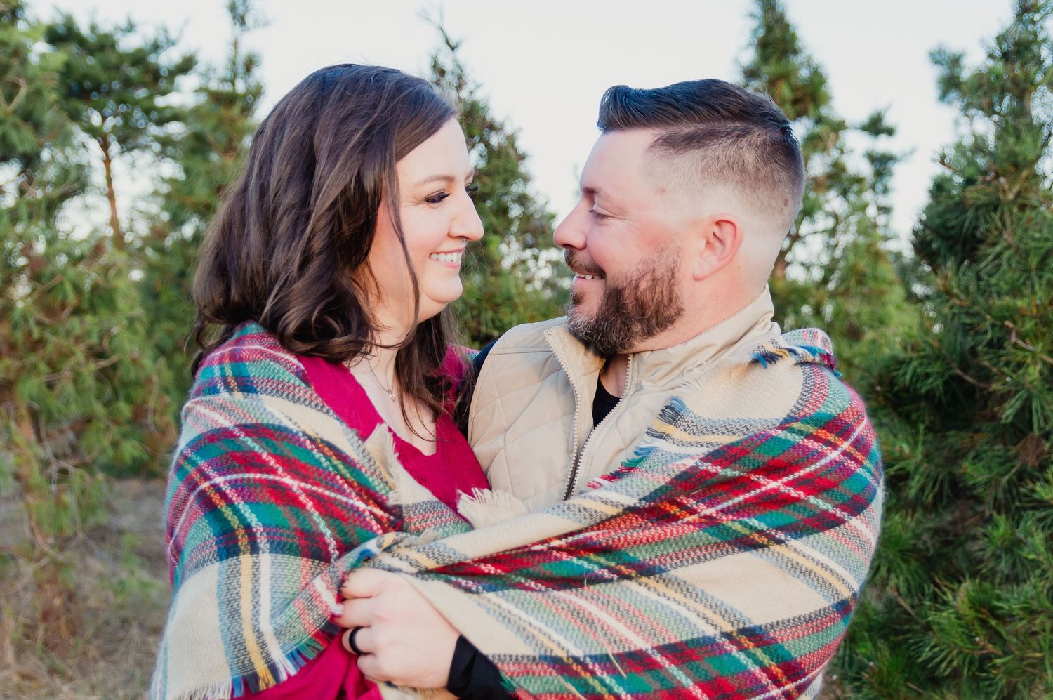Couple wrapped in a plaid blanket sharing an intimate moment outdoors.