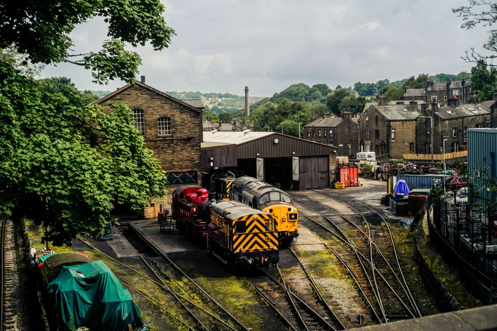 Yellow diesel locomotive at heritage railway station surrounded by brick buildings.