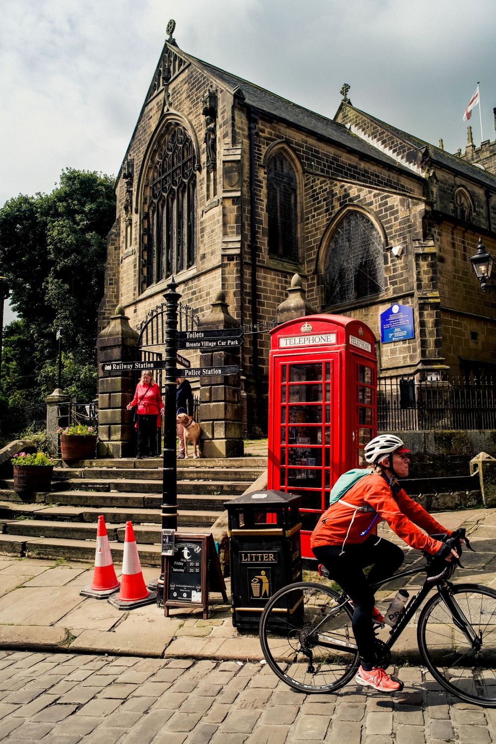 Historic church building with red British phone booth and cyclist passing by.