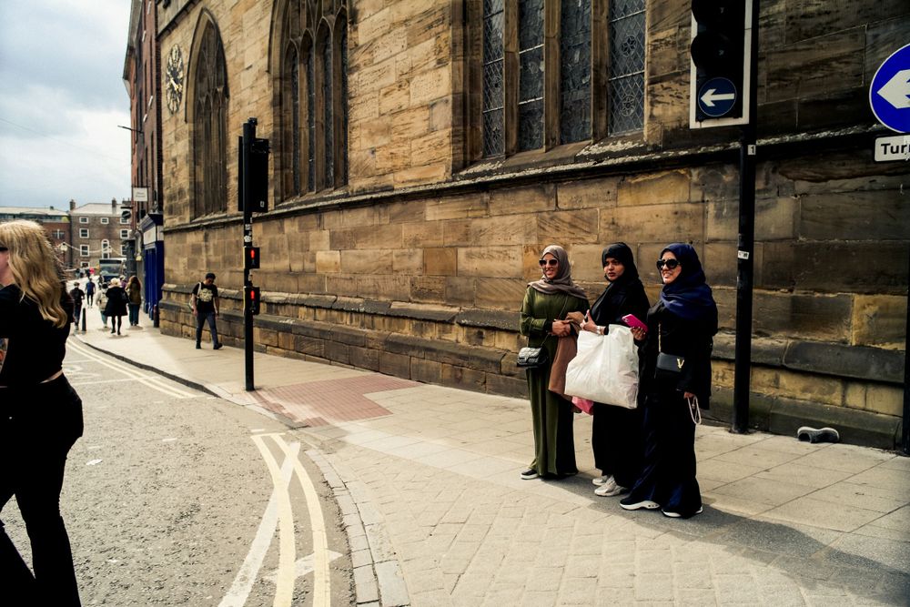 Stone church exterior with pedestrians walking along curved street.