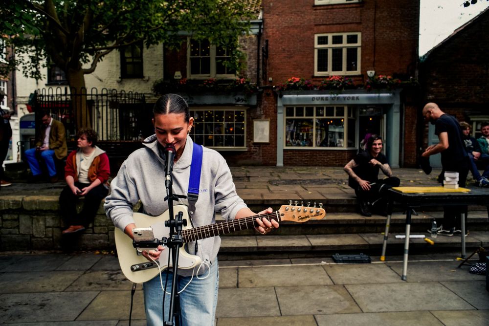 Street musician performing with guitar outside traditional British shops.