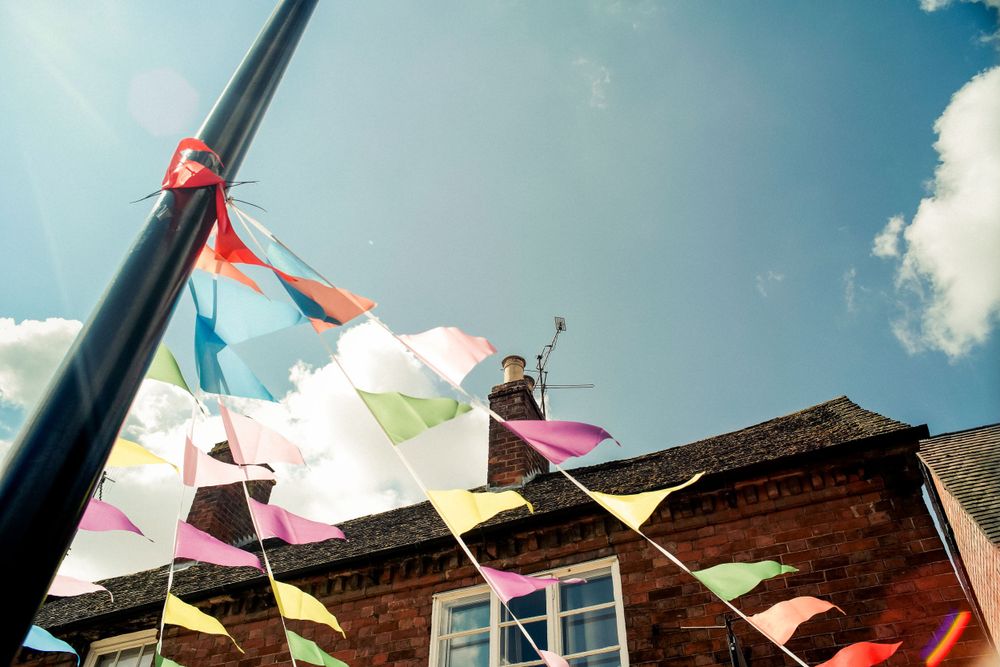 Colorful triangle bunting flags waving against a blue summer sky above traditional buildings.