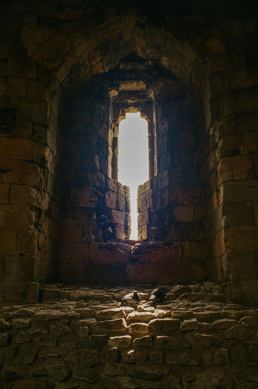 Sunlight streaming through narrow stone window in ancient castle ruins.