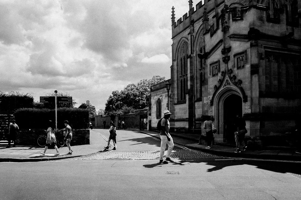 Pedestrians walking near a Gothic church building on a sunny day in black and white.