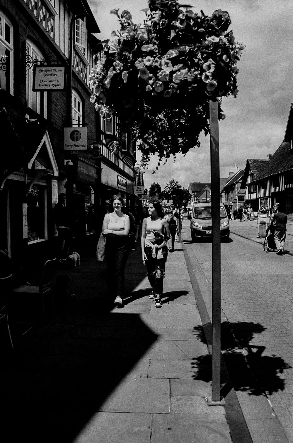 Black and white street scene of a shopping area with decorative hanging flowers.
