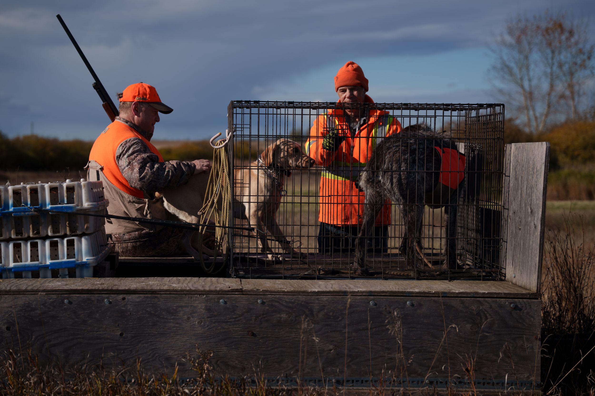 Workers in orange safety gear install black metal fencing on a concrete foundation at a construction site.